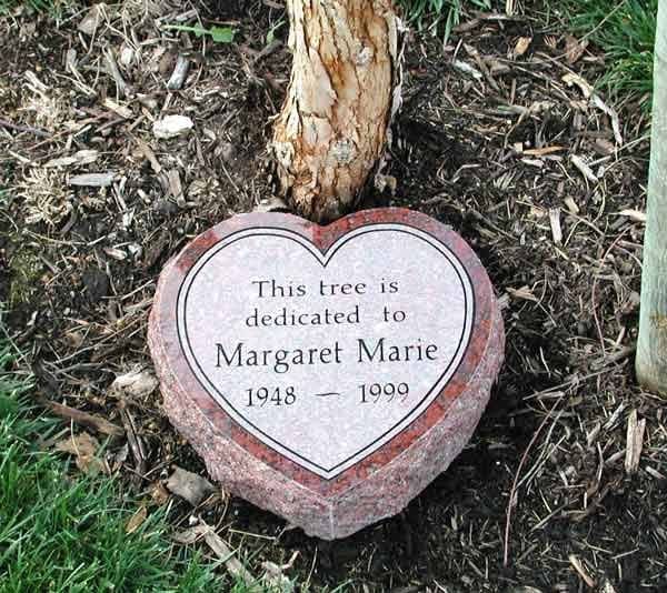 Heart-shaped red granite garden memorial stone at the base of a dedicated tree, engraved for Margaret Marie (1948-1999)
