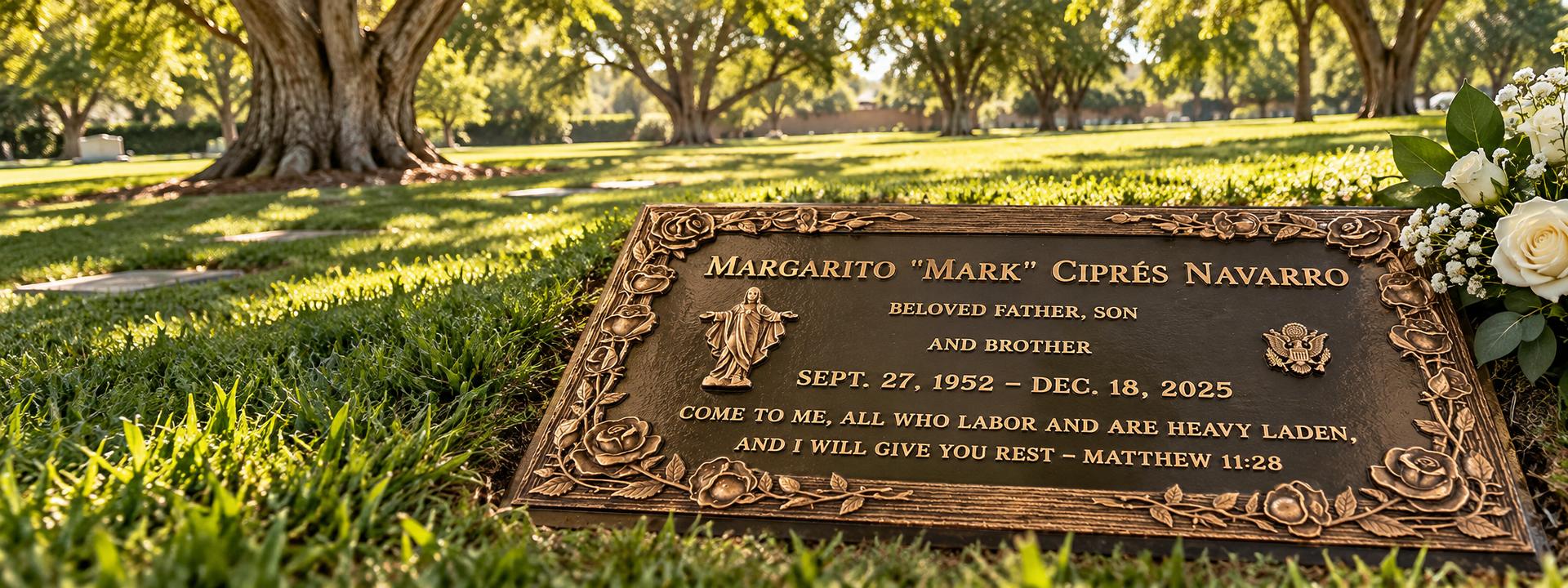 Flat bronze grave marker with a raised rose border and a figure of Jesus, set in the lawn of a tree-lined cemetery, Navarro family